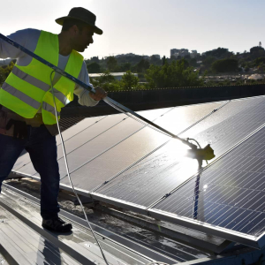 Professionnel photovoltaïque en train de nettoyer des panneaux solaires avec une perche télescopique