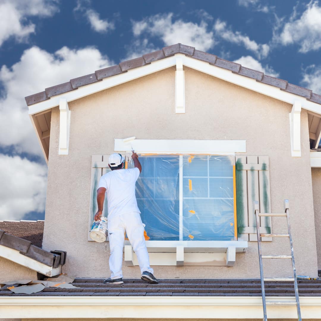 Un monsieur est en train de peindre l'extérieur d'une maison en blanc